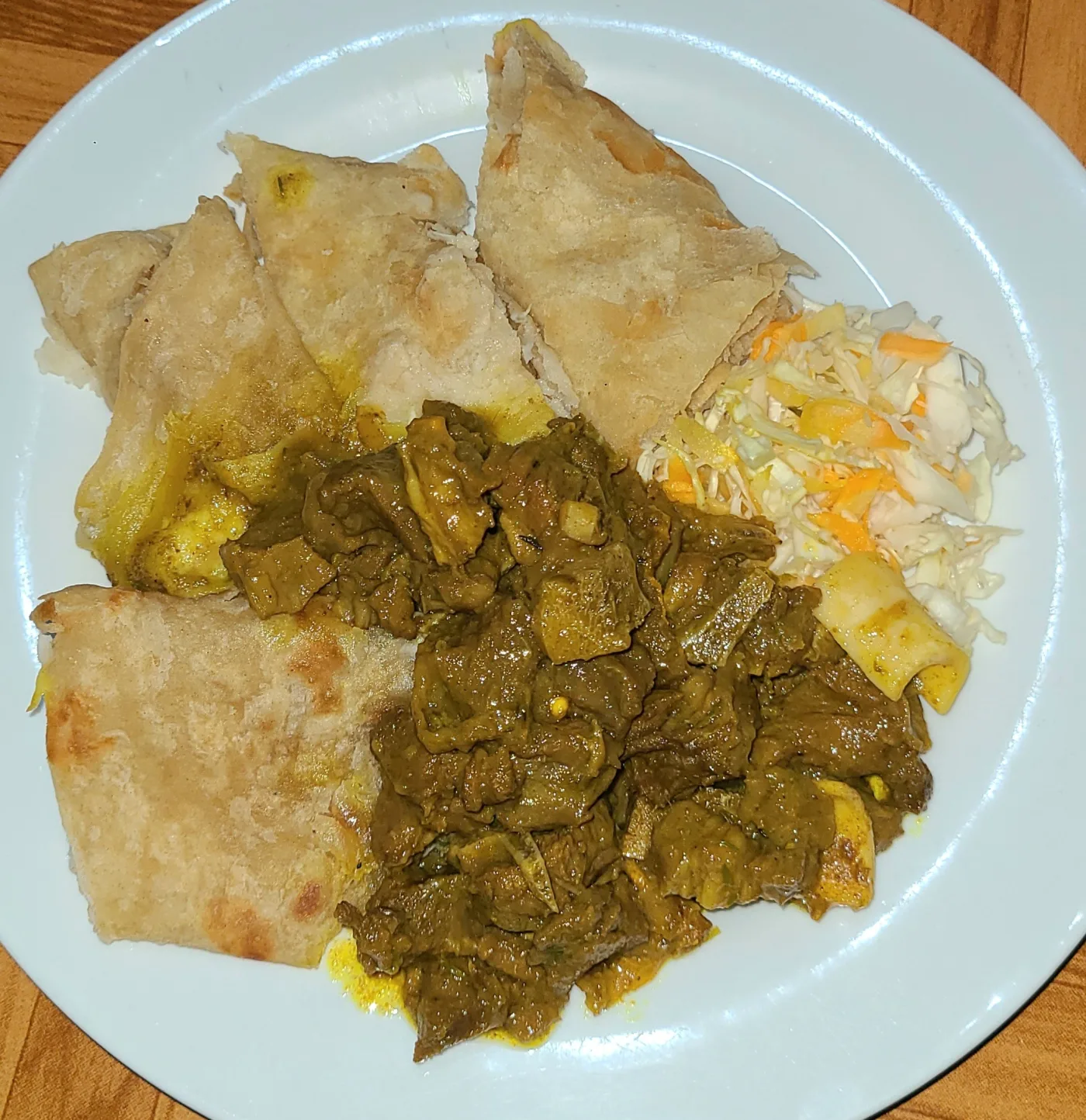 A plate of Jamaican curry goat with roti and coleslaw