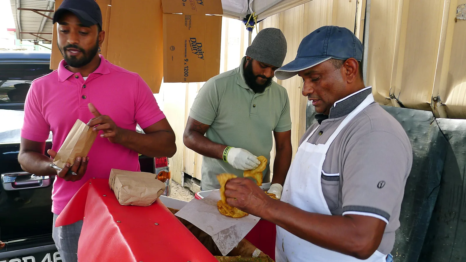 Three men preparing and buying doubles from a street stall in Trinidad and Tobago