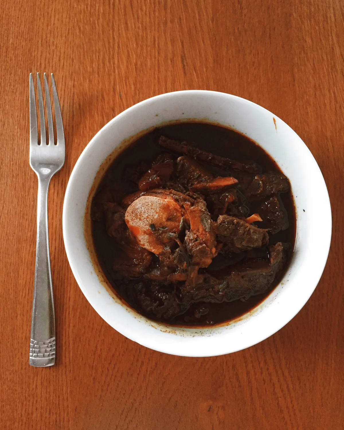 A bowl of dark Guyanese pepperpot stew on a wooden table