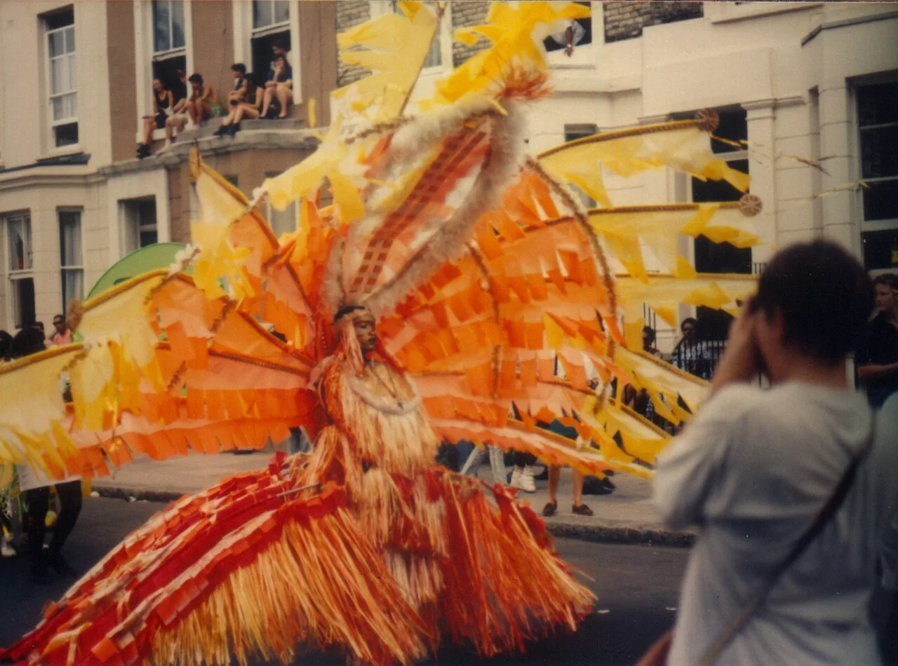 An orange-feathered masquerader moving through the Notting Hill Carnival crowd in 1989