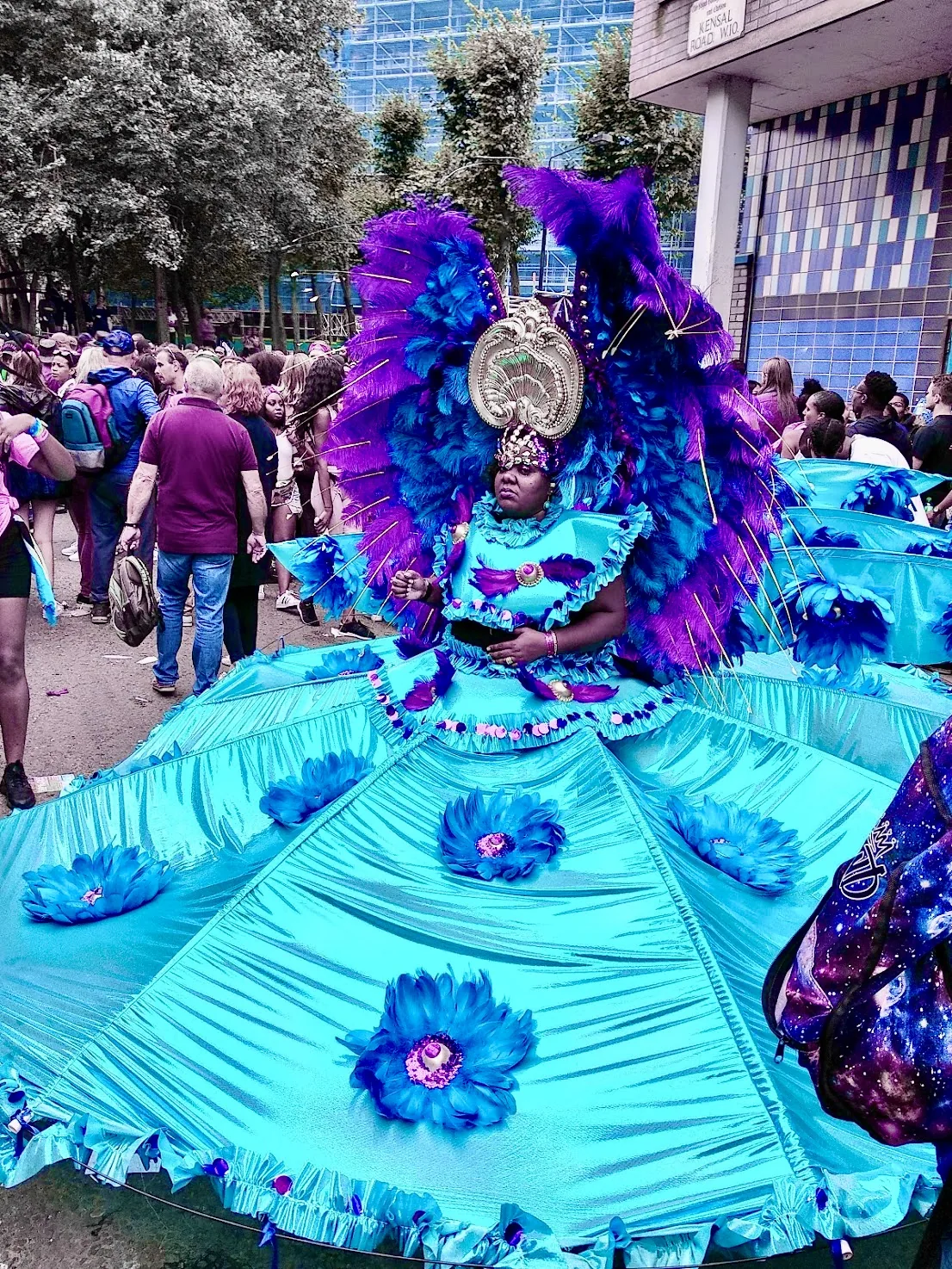 A Black woman playing mas in a vast turquoise and purple traditional Carnival costume on Kensal Road