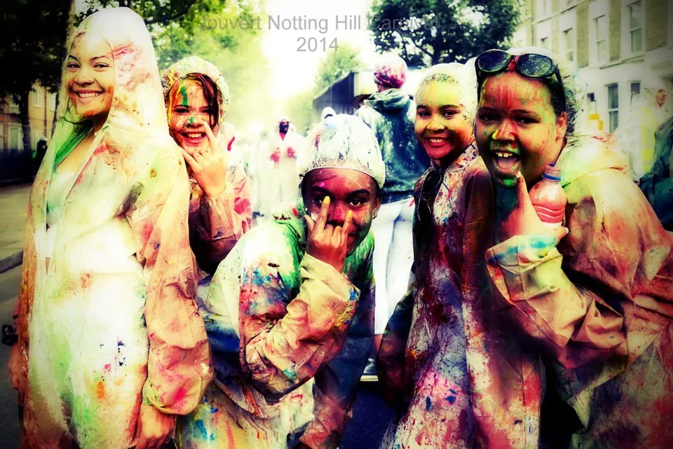 A group of Black women covered in coloured paint smiling together at Notting Hill Carnival J’ouvert