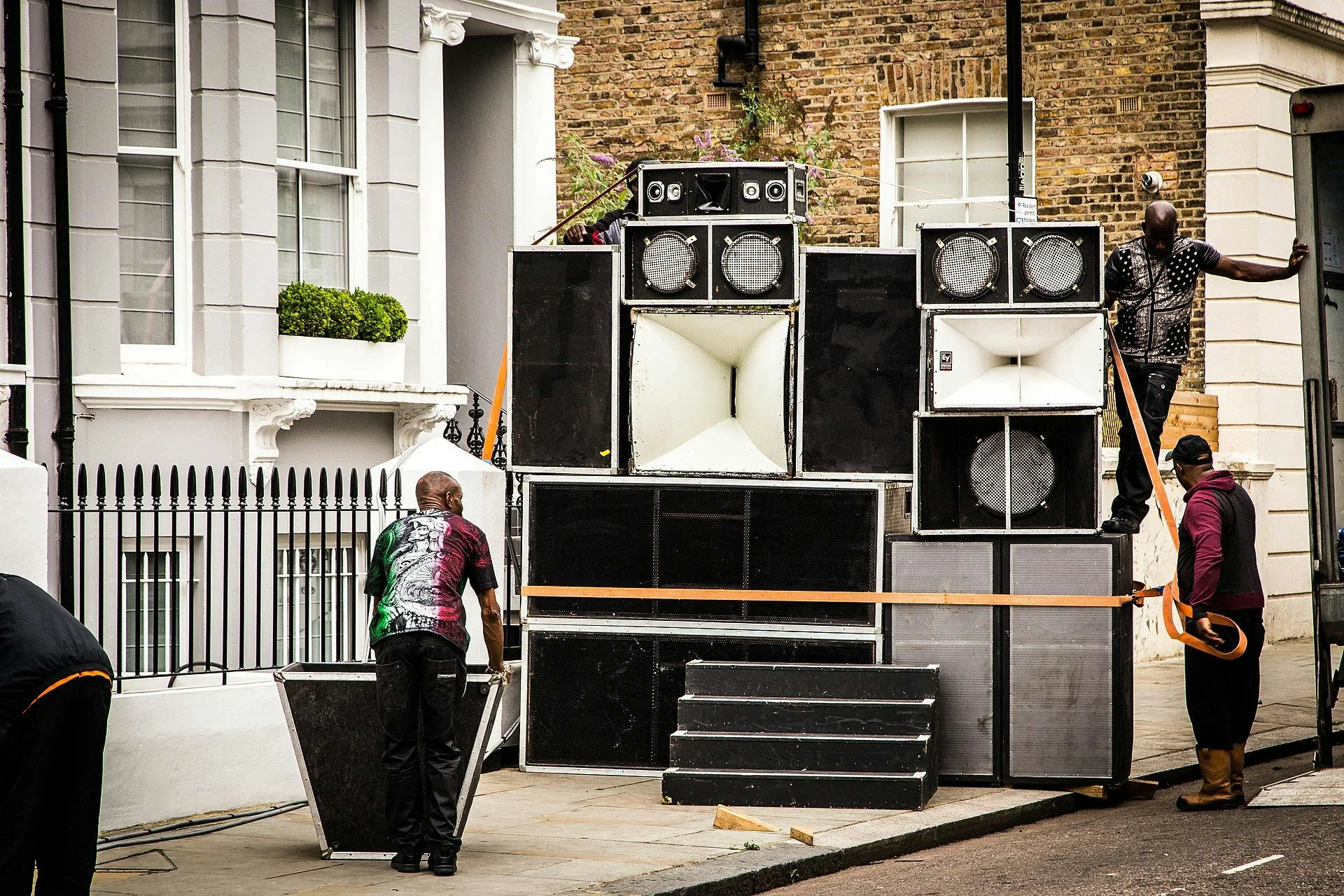 A Black sound-system crew assembling and strapping a large speaker stack on a Notting Hill street