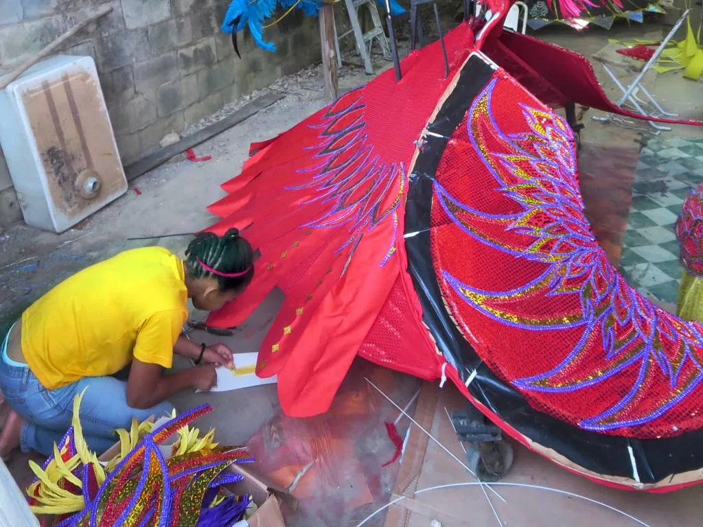 A costume maker working by hand on a large red wire and fabric mas structure in Port of Spain