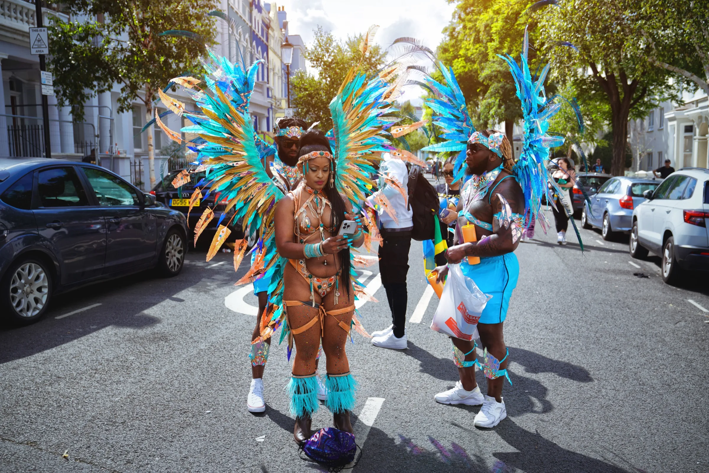 Three masqueraders in turquoise and bronze costumes preparing on a Notting Hill street