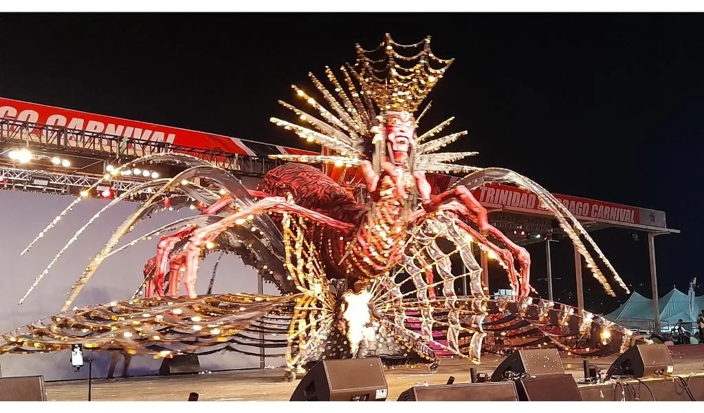 A masquerader performing beneath a huge illuminated spider-shaped Queen costume in Trinidad